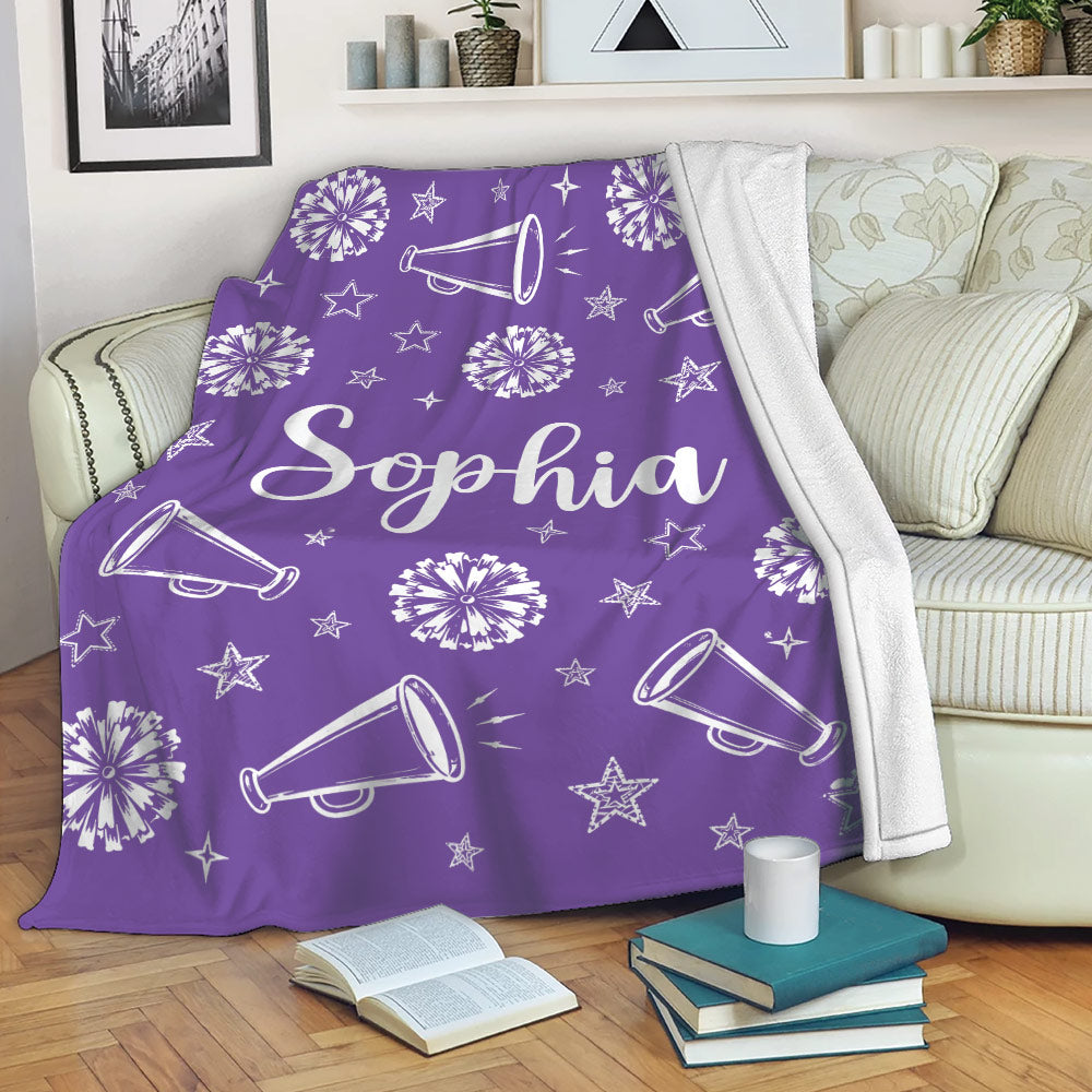 Purple cheerleading throw blanket draped over a sofa with pom-poms, megaphones, and stars