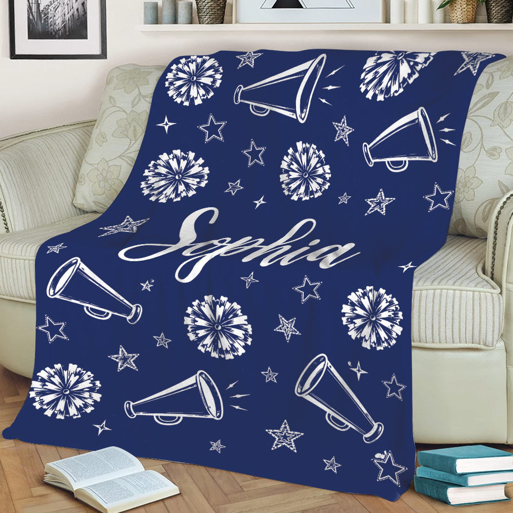 Navy blue cheerleading throw blanket displayed on a sofa with pom-poms, megaphones, and stars