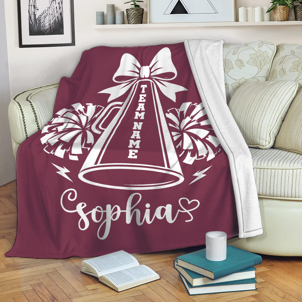 Maroon cheerleading blanket displayed on a sofa with megaphone and pom-pom design