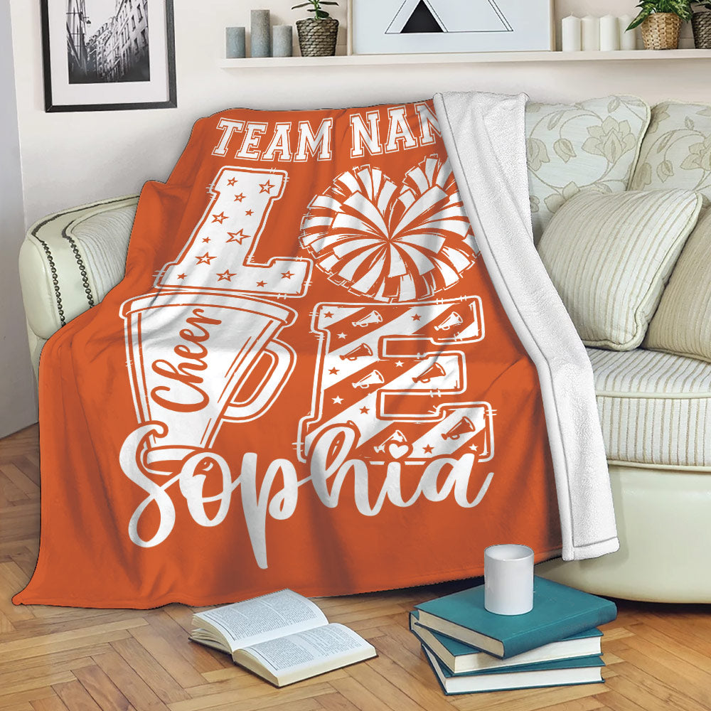 Orange cheerleading throw blanket styled on a sofa with pom-pom and megaphone artwork
