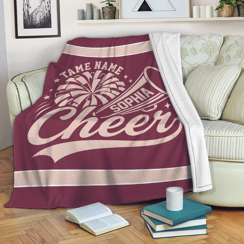 Maroon cheerleading throw blanket draped over a sofa with megaphone and pom-pom artwork