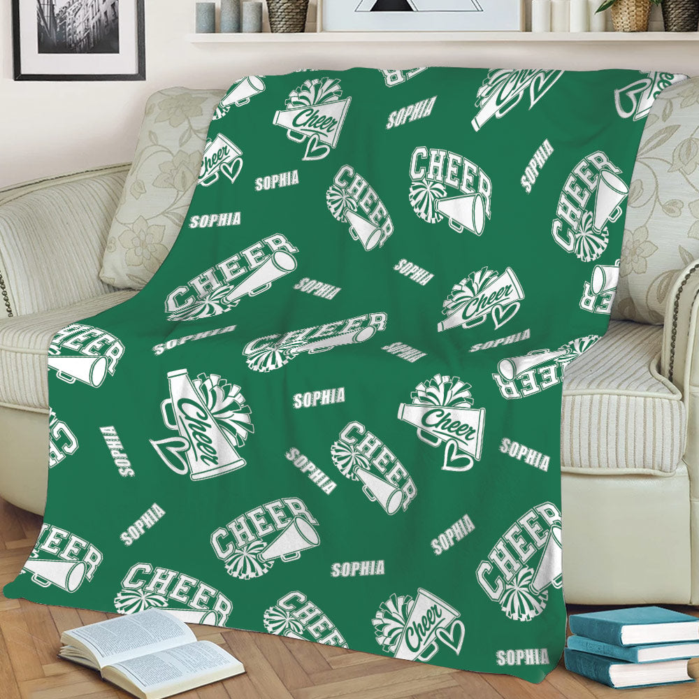 Green cheerleading blanket displayed on a sofa with repeating white cheer artwork