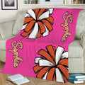 Bright pink cheerleading blanket with bold orange and white pom-pom artwork on a sofa