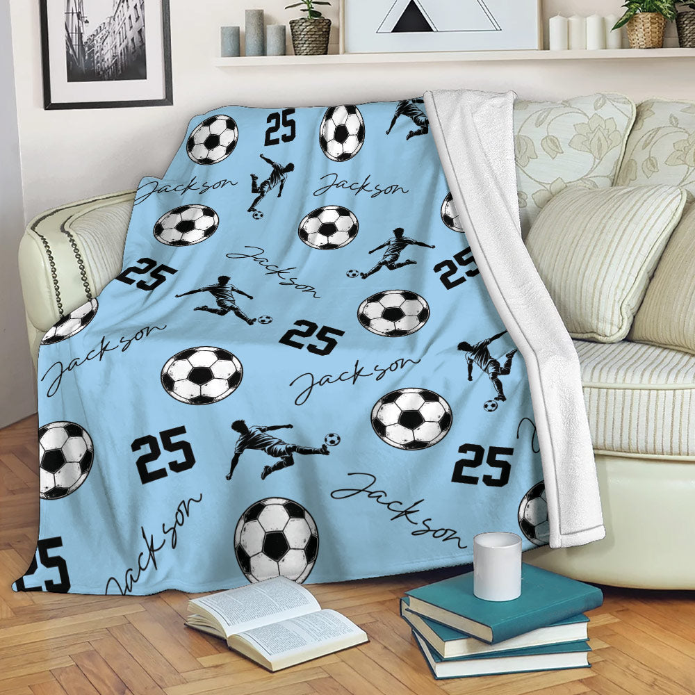 Light blue soccer throw blanket styled on a sofa with soccer balls and kicking player silhouettes