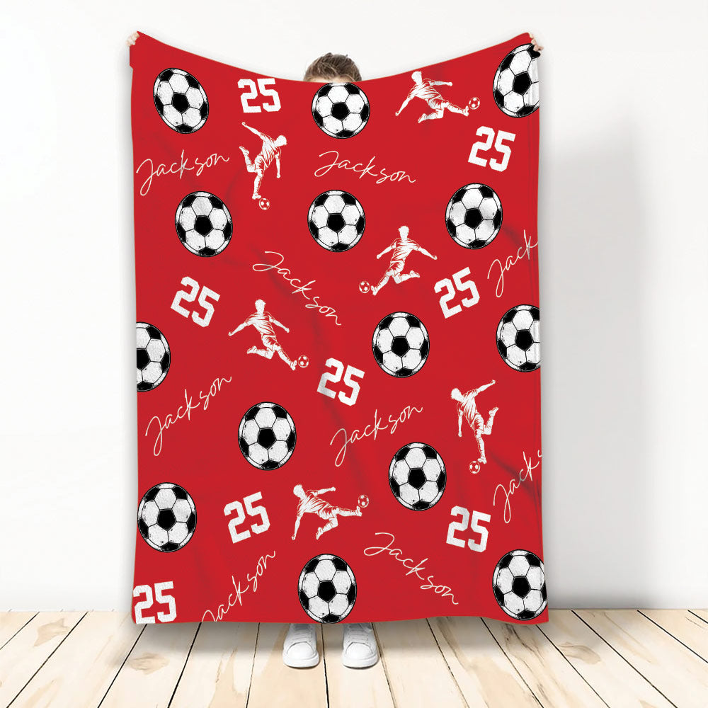 Red soccer blanket displaying soccer balls and dynamic player silhouettes in a bold repeating pattern