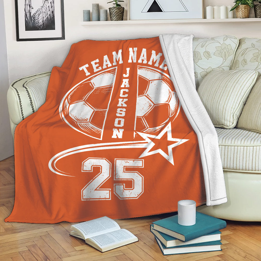 Orange soccer throw blanket draped over a sofa with soccer ball artwork and sporty team design