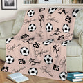 Blush pink soccer throw blanket displayed on a sofa with soccer balls and female soccer artwork