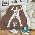 Soccer player throw blanket displayed on a couch with a bold brown background and soccer ball artwork