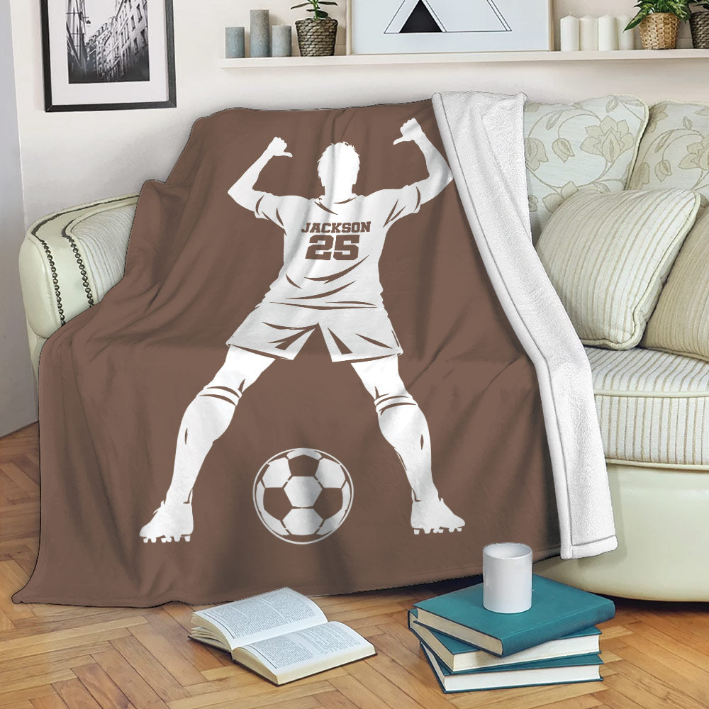 Soccer player throw blanket displayed on a couch with a bold brown background and soccer ball artwork