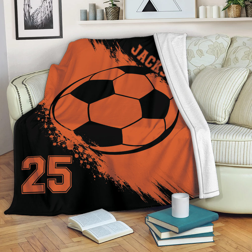 Orange and black soccer throw blanket draped over a sofa with bold ball artwork