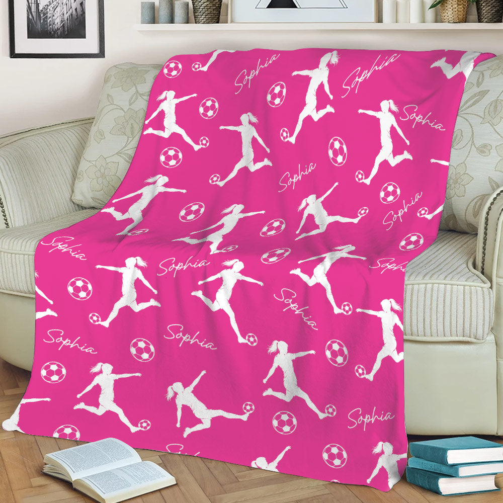Pink soccer throw blanket styled on a sofa with energetic player silhouettes and repeating soccer balls