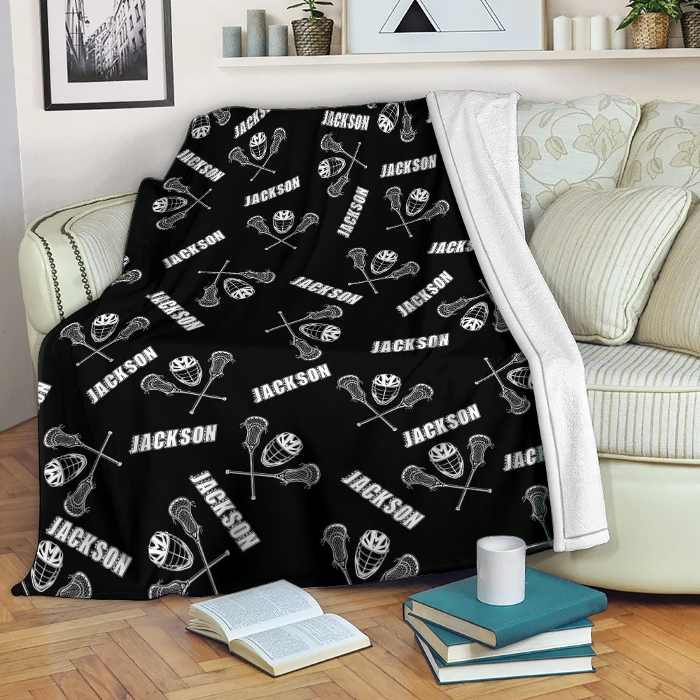 Black lacrosse throw blanket draped across a sofa with repeating sticks, helmets, and balls