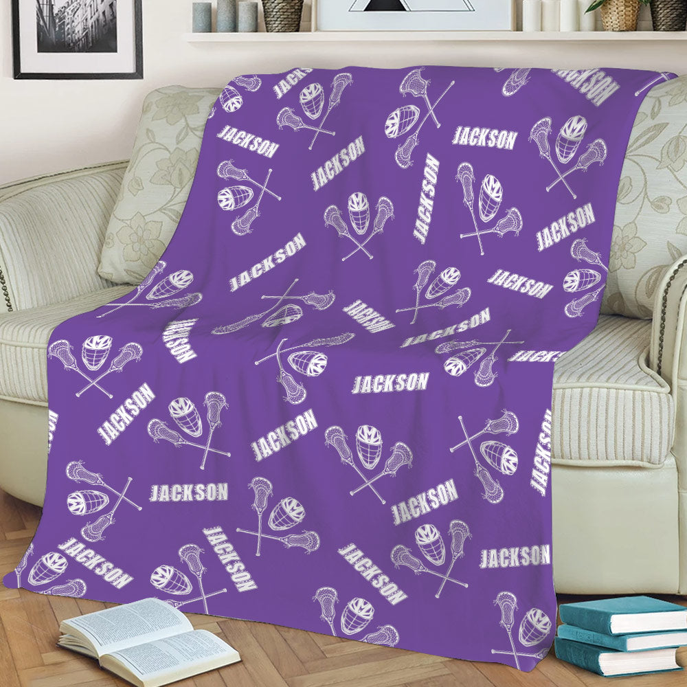 Purple lacrosse throw blanket spread across a sofa with repeating sticks, helmets, and balls