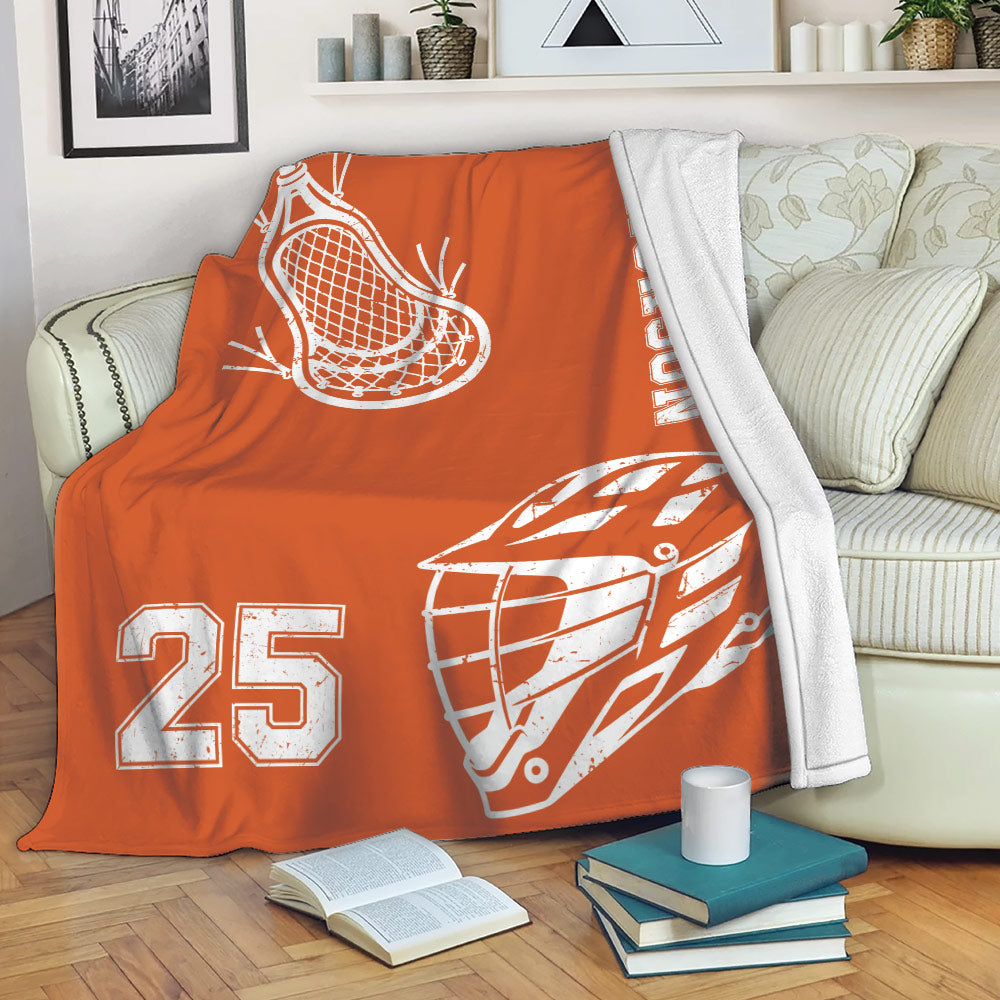 Orange lacrosse blanket draped over a sofa with helmet, stick, and sports number artwork