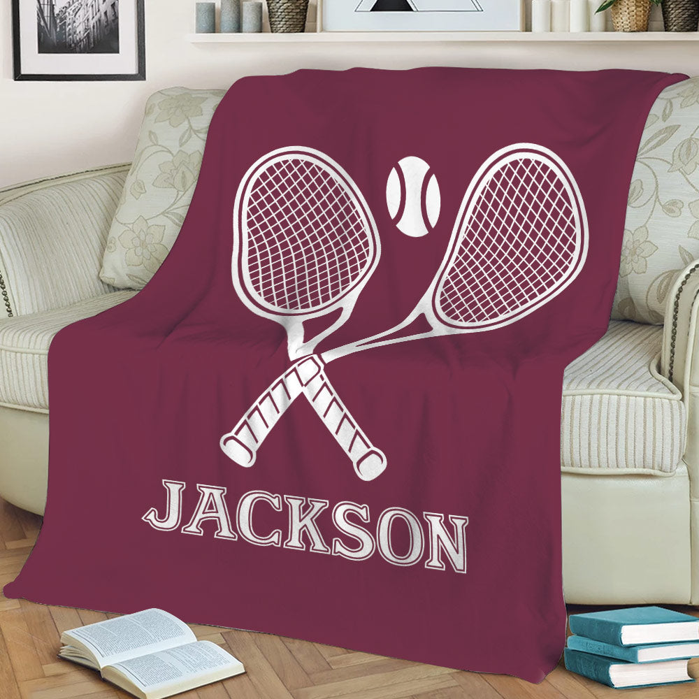 Maroon tennis throw blanket displaying crossed racquets and tennis ball artwork on a sofa