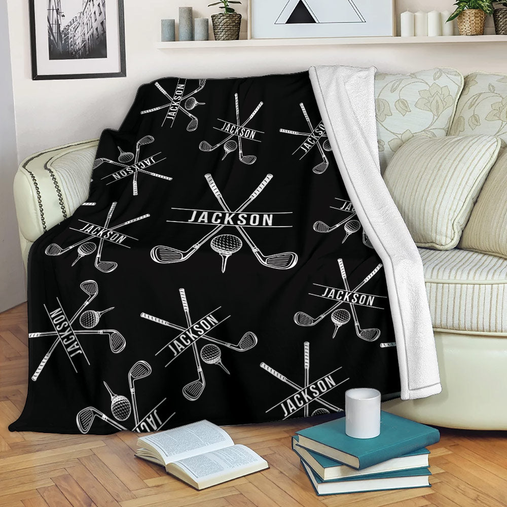 Black golf throw blanket draped over a sofa with repeating crossed clubs and golf ball design