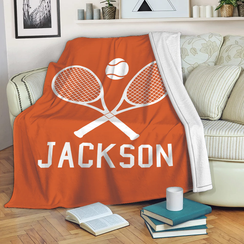Orange tennis throw blanket draped over a sofa with crossed racket and tennis ball artwork