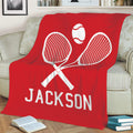 Red tennis throw blanket displayed on a sofa with bold crossed racket and tennis ball artwork