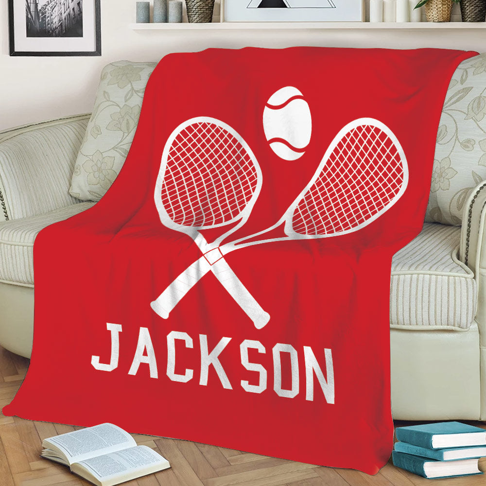 Red tennis throw blanket displayed on a sofa with bold crossed racket and tennis ball artwork