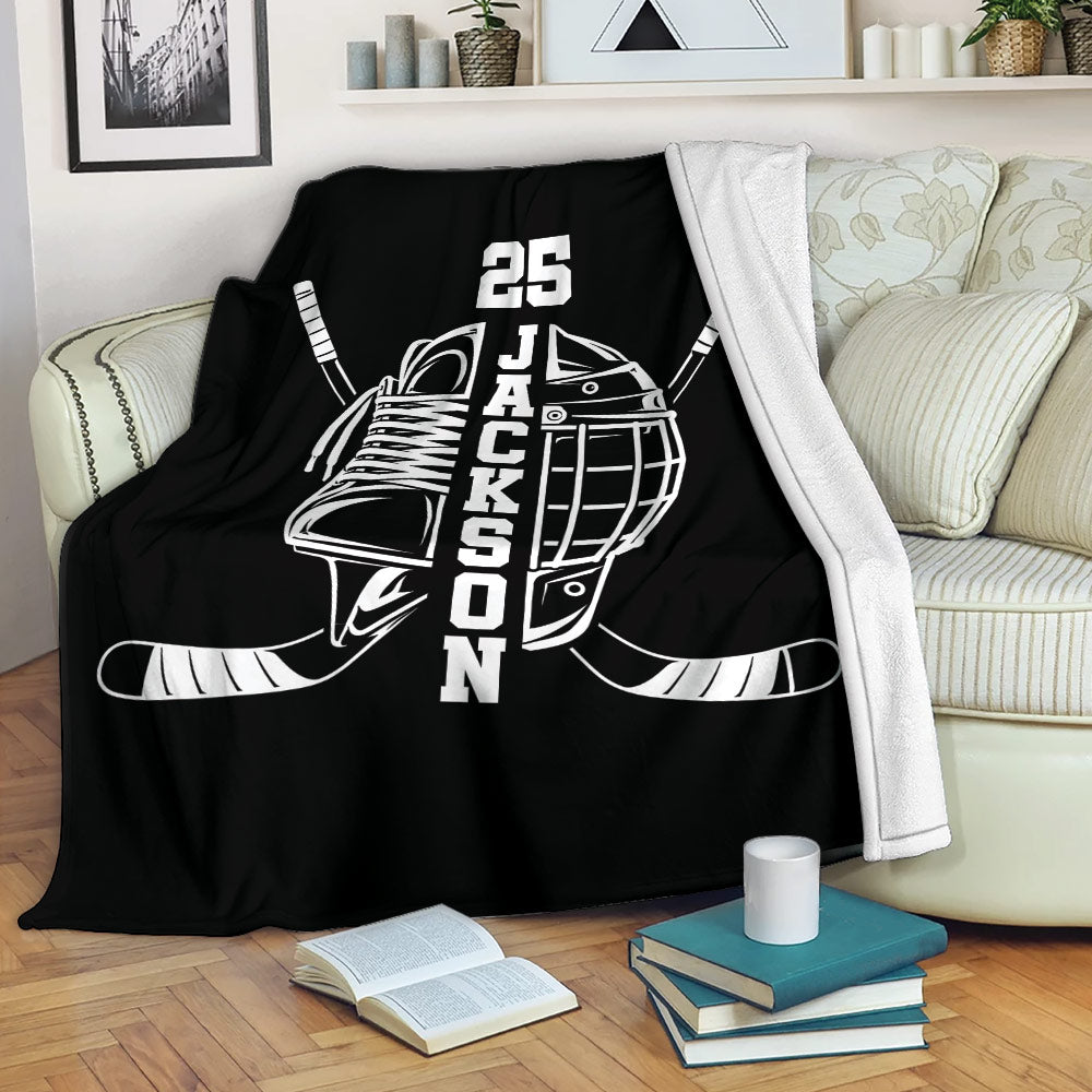 Black hockey blanket draped over a sofa with skate, helmet, and crossed hockey sticks design