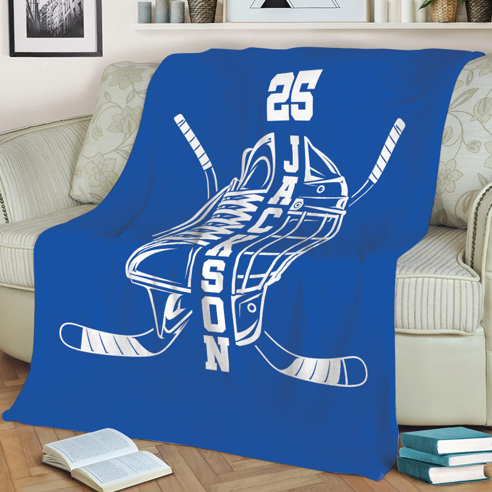 Blue hockey blanket styled on a sofa with skate, helmet, and crossed hockey stick artwork