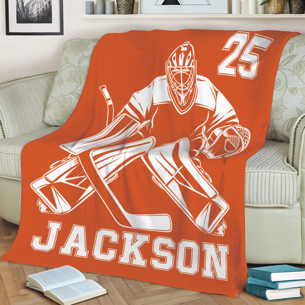 Orange hockey goalie throw blanket displayed across a sofa with high contrast sports artwork