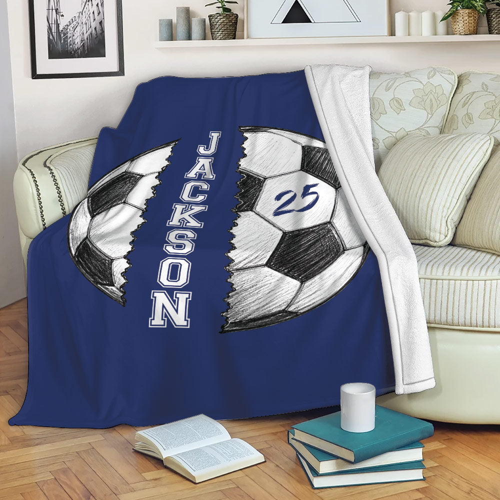 Blue soccer throw blanket displayed across a sofa with split soccer ball artwork and bold vertical design