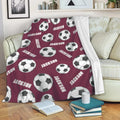 Maroon soccer throw blanket draped over a sofa with repeating black and white soccer ball artwork