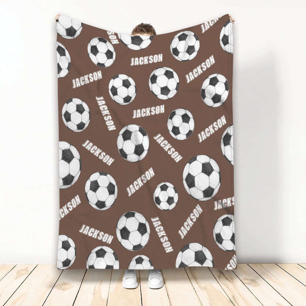 Brown soccer blanket shown upright with a repeating pattern of black and white soccer balls