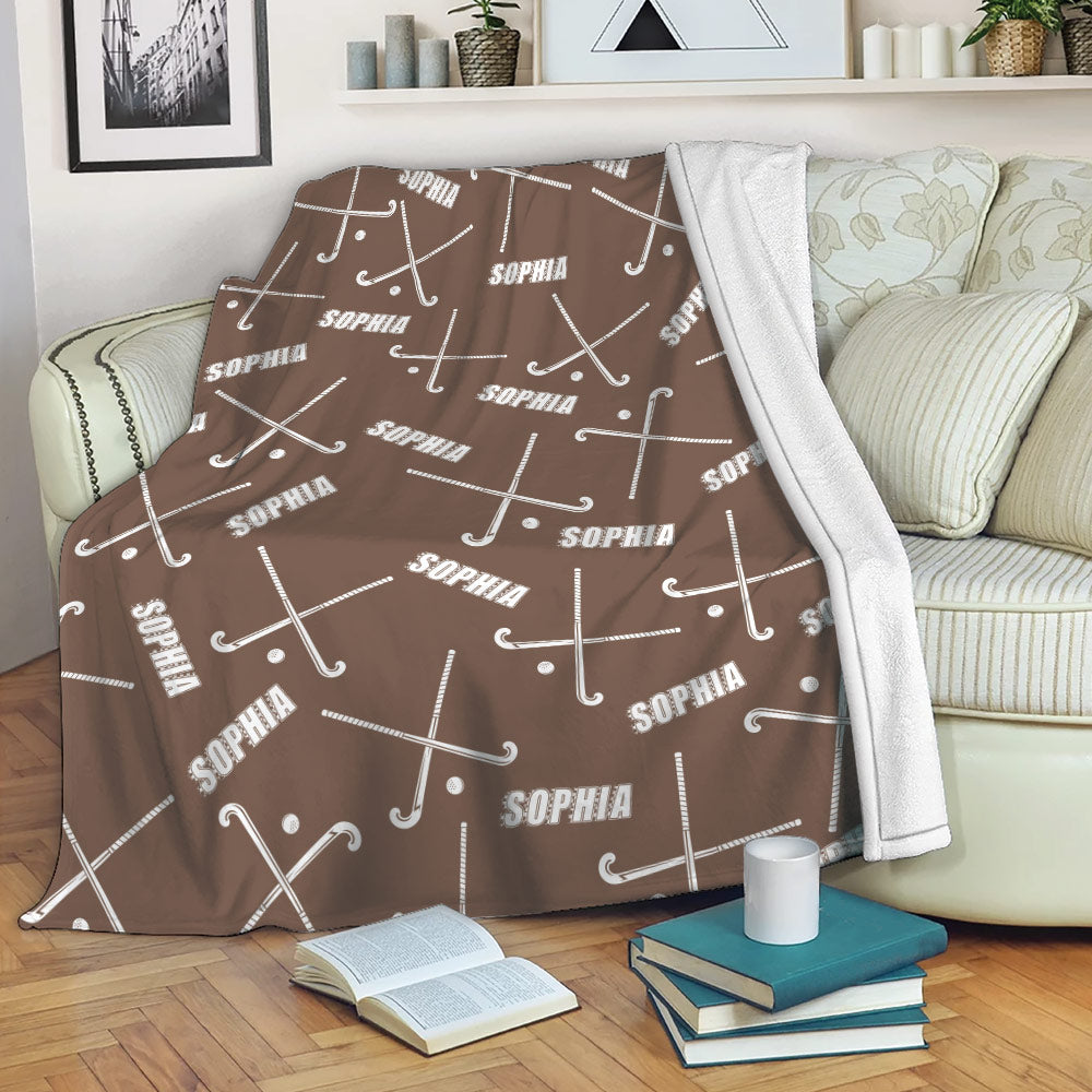 Brown hockey throw blanket draped over a sofa with crossed sticks and pucks in a repeating sports pattern