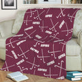 Maroon hockey throw blanket spread across a sofa with white sticks and pucks in a bold sports design