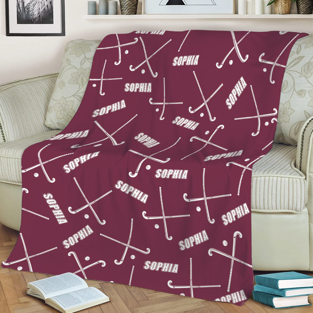 Maroon hockey throw blanket spread across a sofa with white sticks and pucks in a bold sports design