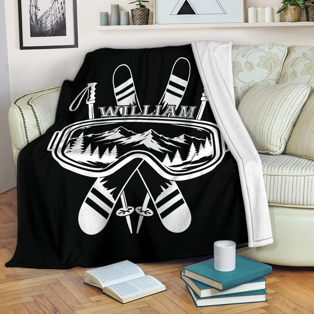 Black skiing blanket displayed on a sofa with crossed skis, goggles, poles, and mountain scenery