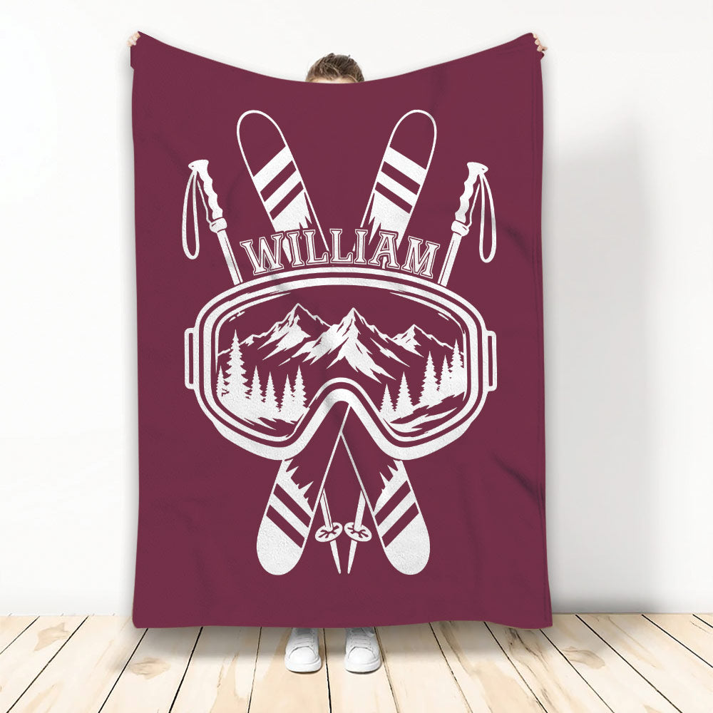 Maroon skiing blanket featuring crossed skis, ski goggles, poles, and a mountain landscape
