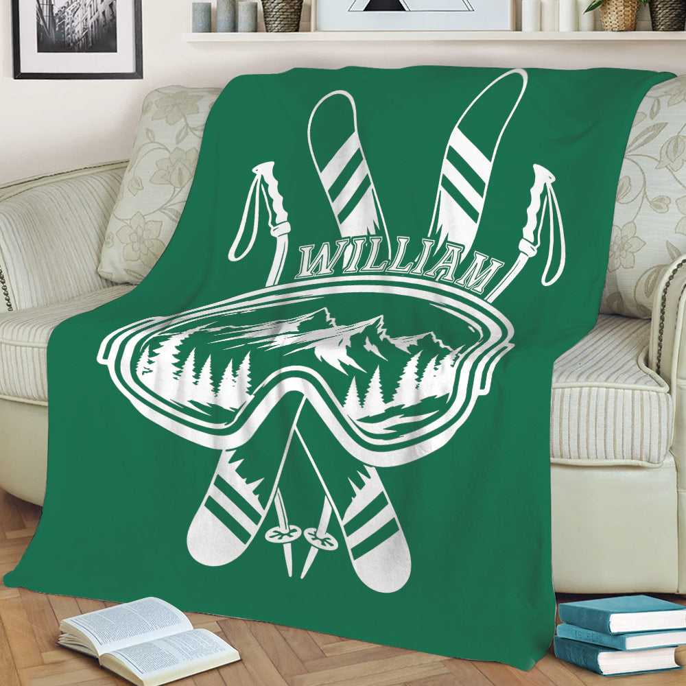 Green skiing throw blanket draped over a sofa with ski goggles, skis, poles, and mountains