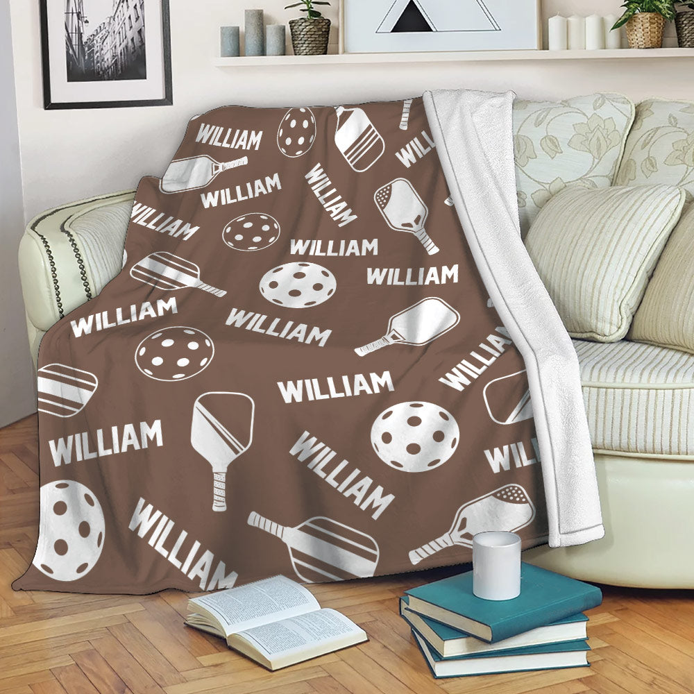 Brown pickleball blanket draped over a sofa with paddle and ball artwork for cozy lounging