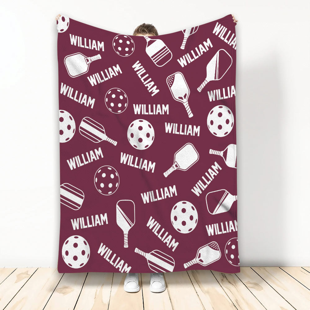 Burgundy pickleball throw blanket displaying repeating paddle and perforated ball illustrations