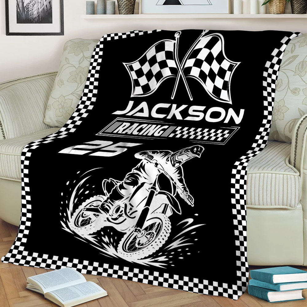 Black motocross blanket displayed on a sofa with dirt bike and racing flag artwork