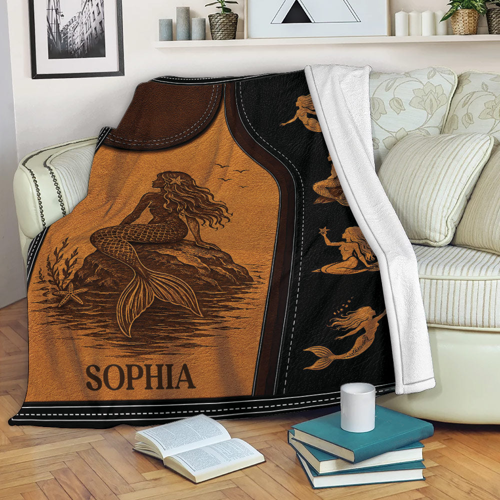 Mermaid throw blanket draped over a sofa, featuring sepia ocean artwork and a black illustrated border