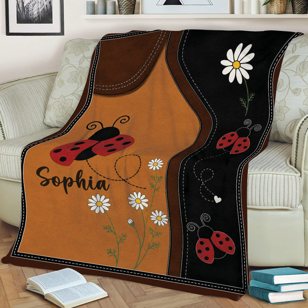 Ladybug throw blanket styled on a couch with playful insects, daisies, and contrasting brown and black panels