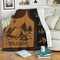 Camping throw blanket displayed on a couch with tent, campfire, pine tree, and compass artwork