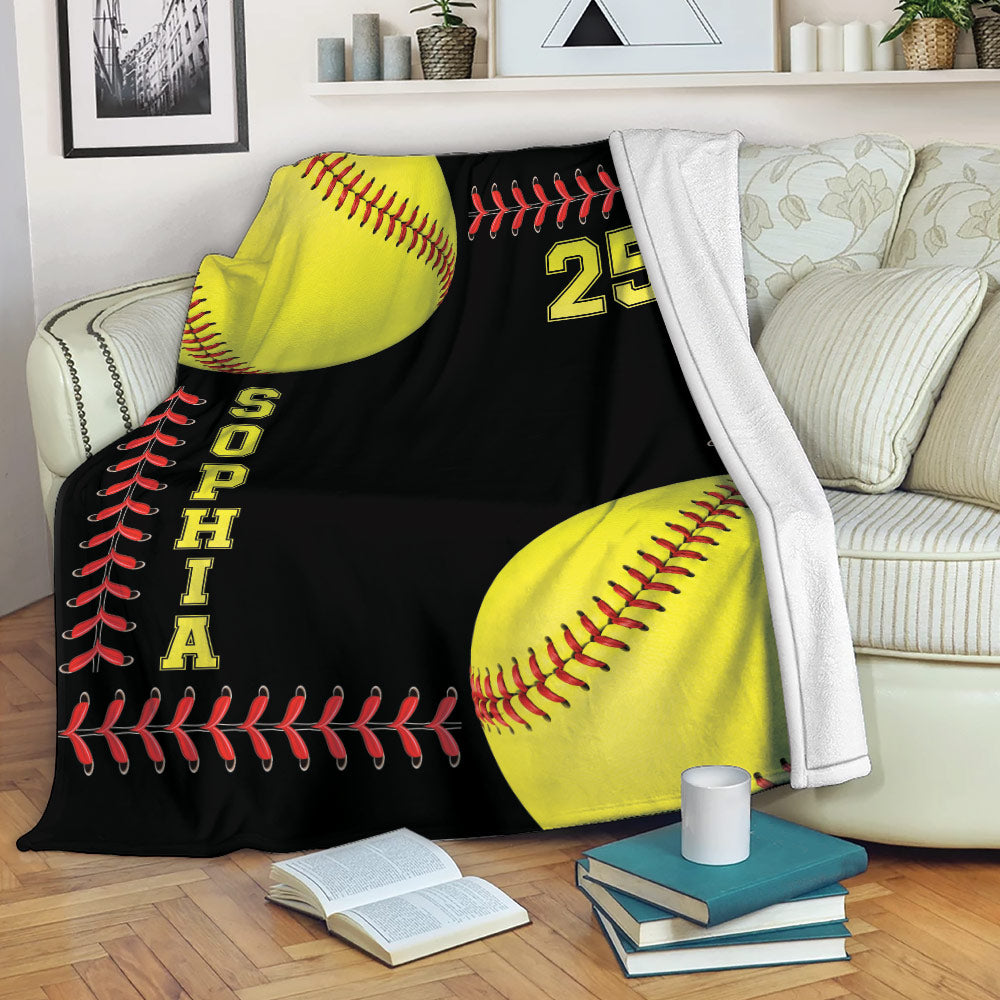 Softball blanket displayed on a sofa with bright yellow softballs and red stitching on a black background