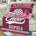 Pink and maroon cheerleading blanket displayed on a sofa with pom-pom and megaphone artwork