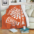 Orange cheerleading throw blanket displayed on a sofa with pom-pom and megaphone design