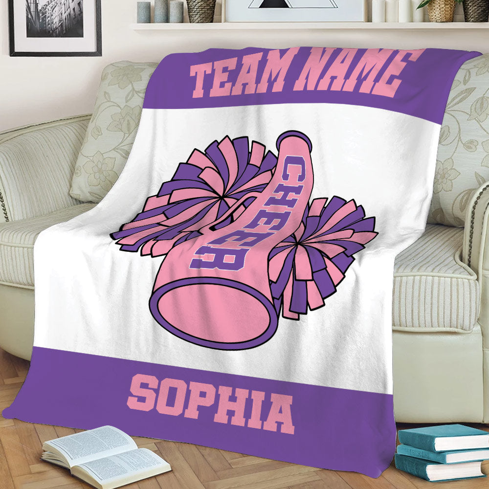 Pink and purple cheerleading blanket displayed on a sofa with pom poms and megaphone
