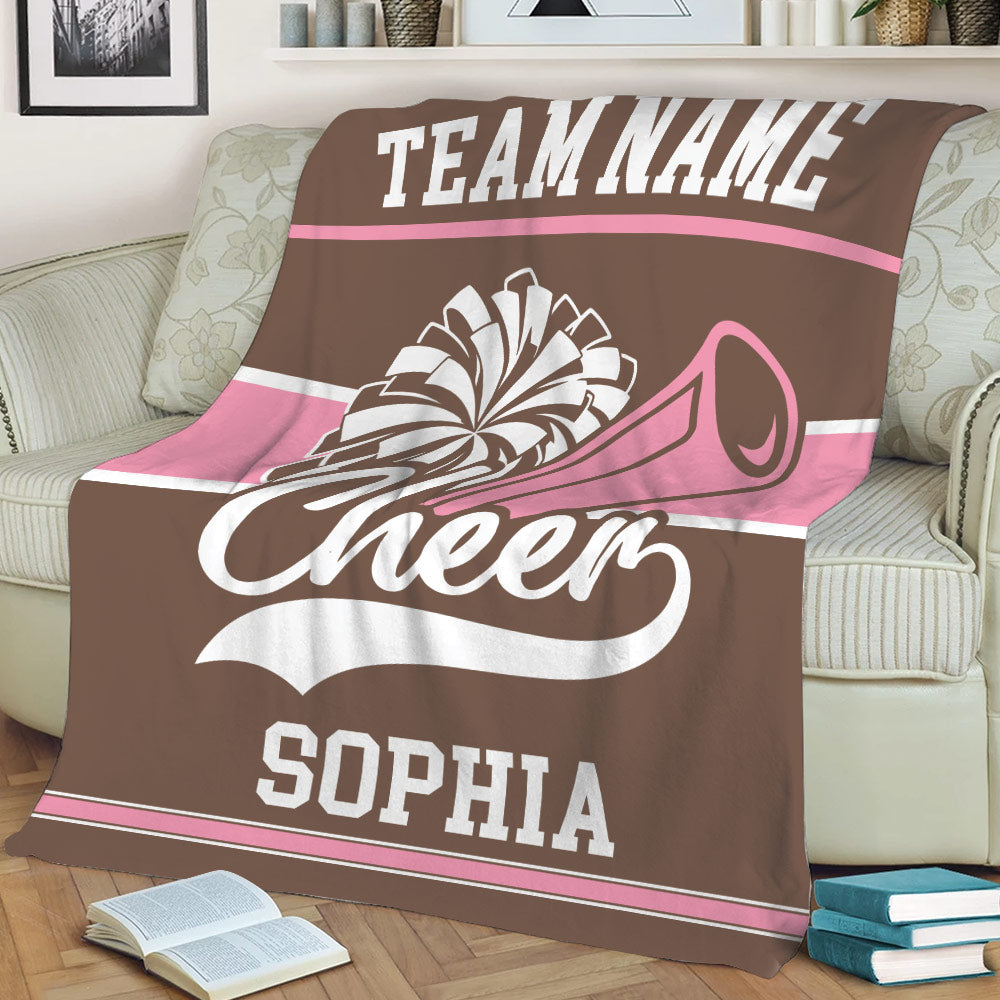 Brown and pink cheerleading throw blanket styled across a sofa with pom-pom and megaphone artwork