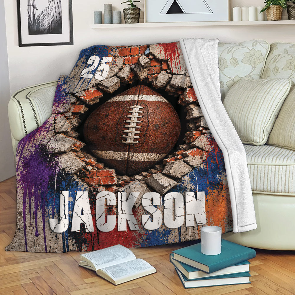 Football throw blanket displayed on a sofa, featuring cracked concrete, brick textures, and vivid sports artwork