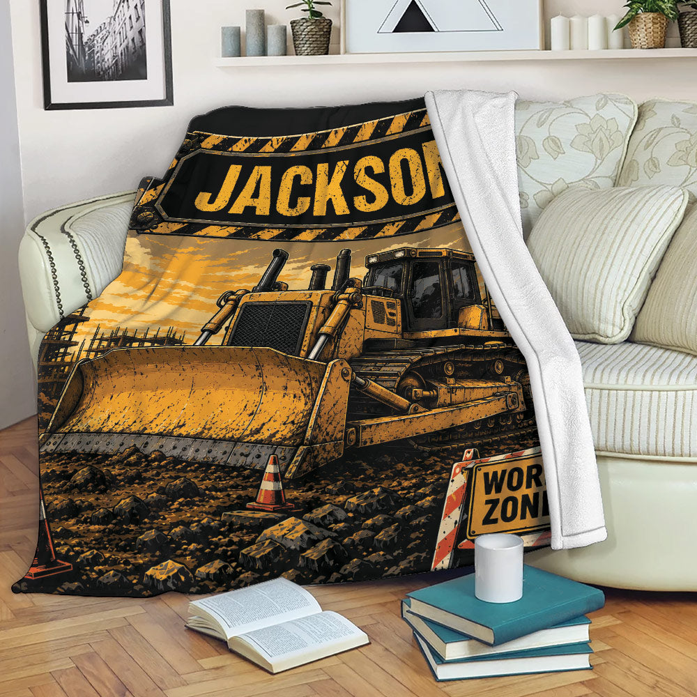 Construction truck throw blanket displayed on a sofa with bulldozer artwork, work-zone details, and warm industrial colors