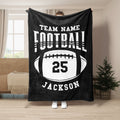 Black football throw blanket displayed in a living room with contrasting white sports artwork