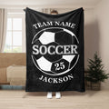 Black soccer throw blanket held indoors with bold white soccer ball artwork